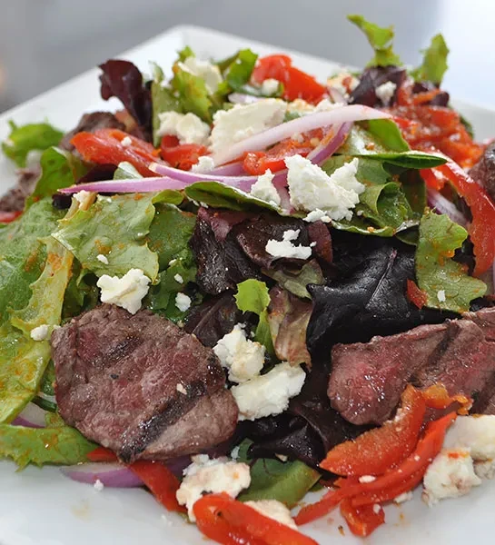 Top-down view of a steak salad with greens, feta, and peppers.