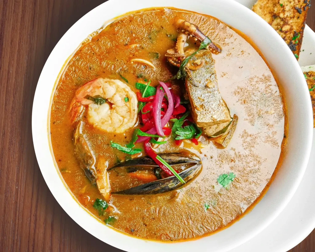 Close-up of seafood stew with shrimp, mussels, fish, and squid in a white bowl.