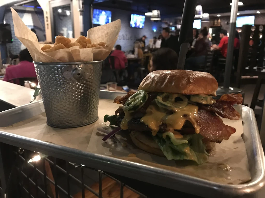 Large burger with cheese, bacon, jalapeños, knife, and tots.