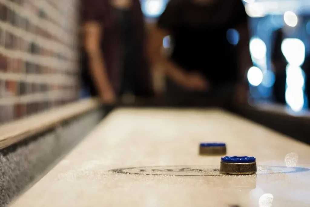 Low-angle view: two blue shuffleboard pucks, blurred people behind.