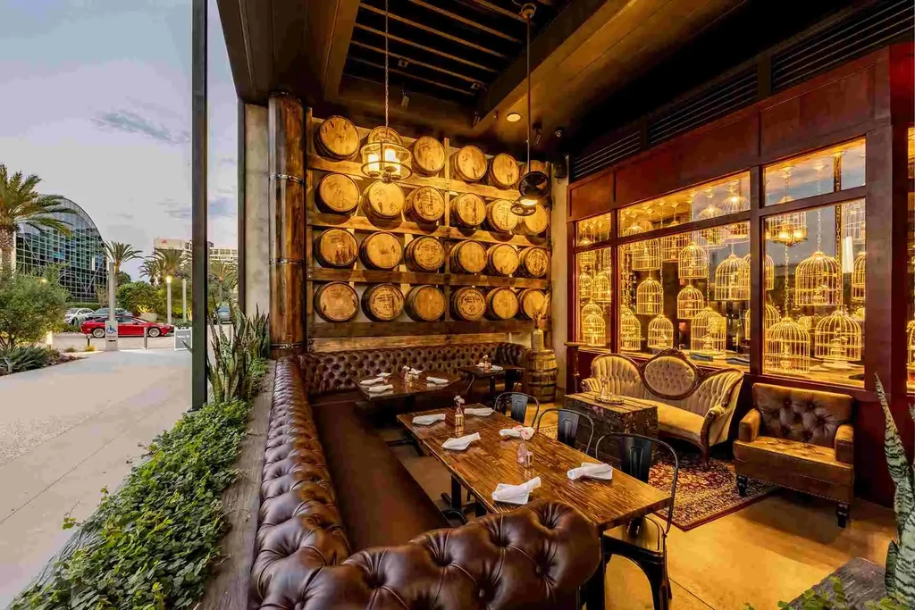 Empty restaurant with barrel wall, glowing birdcages, and modern outdoor view.