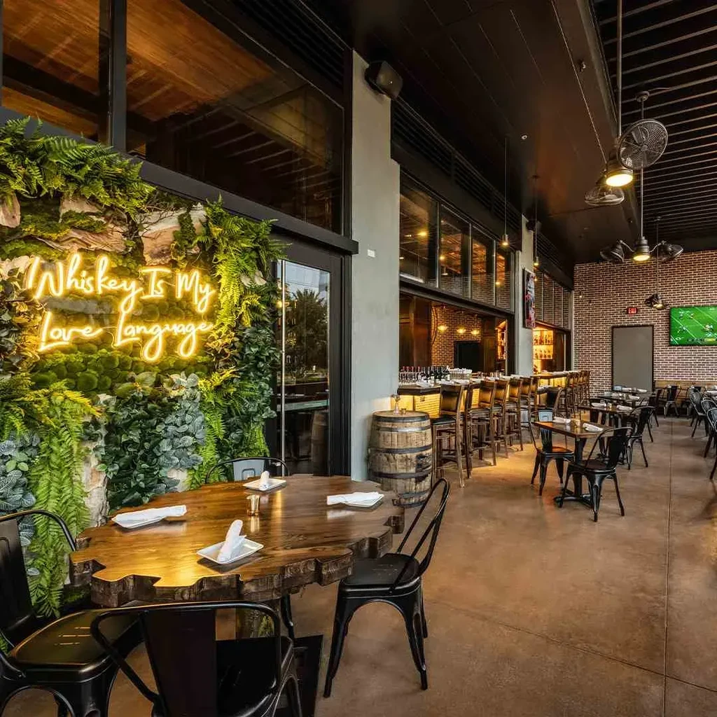 Restaurant interior with "Whiskey Is My Love Language" neon sign on a green wall.