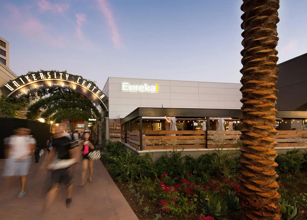 Modern Eureka! restaurant at dusk, with patio, palm, and lighted archway.