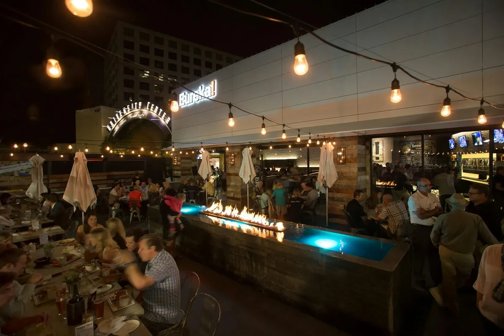 Eureka! restaurant patio at night with patrons, string lights, fire pit.