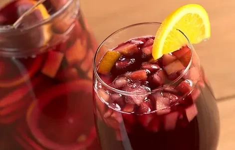 Glass of red fruit drink with diced fruit and an orange slice.