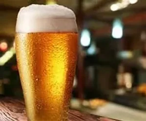 Cold golden beer with a thick frothy head on a wooden surface.