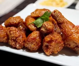 Crispy golden-brown fried chicken on a white plate with a green garnish.