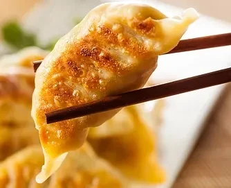 Crispy golden-brown pan-fried dumpling held mid-air by chopsticks.