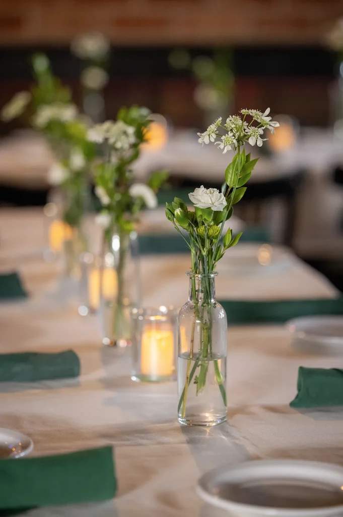 Table setting with white flowers, lit candles, green napkins.