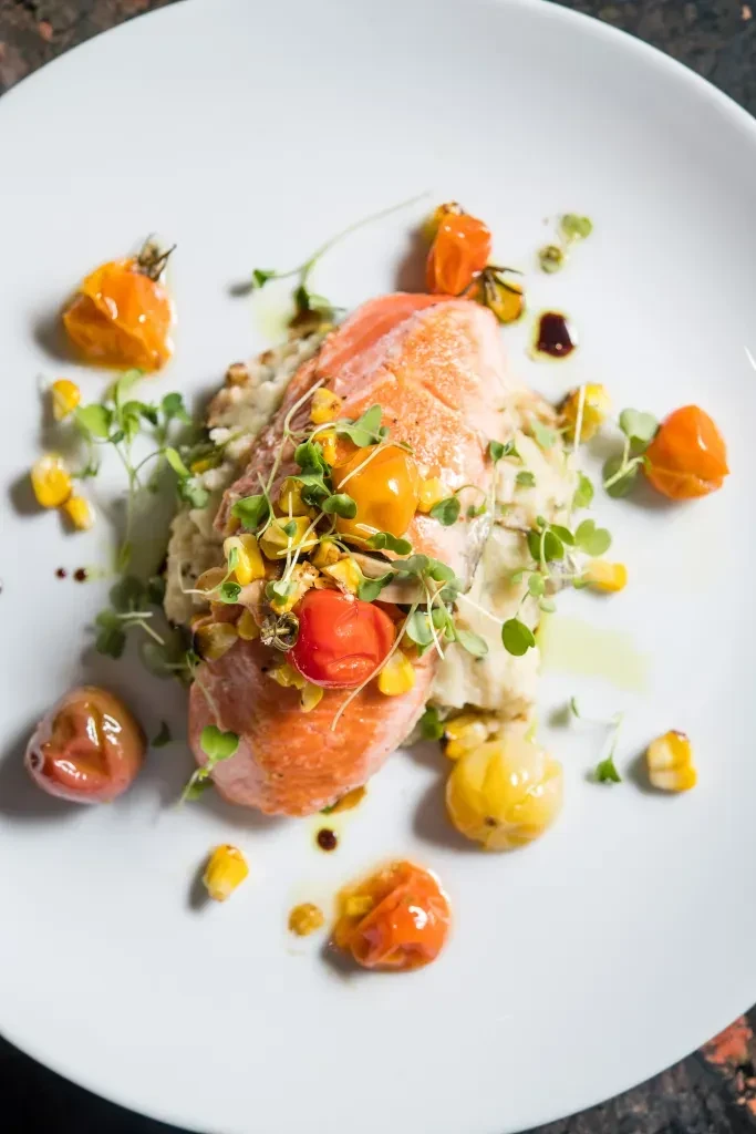 Plated salmon fillet, potatoes, cherry tomatoes, corn, and microgreens.