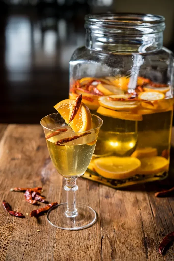 Rustic still life with jar and cocktail glass of amber citrus-chili drink.