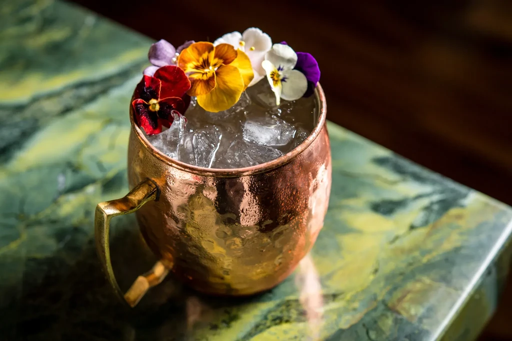 Hammered copper mug cocktail with colorful pansy flowers on a green marble counter.