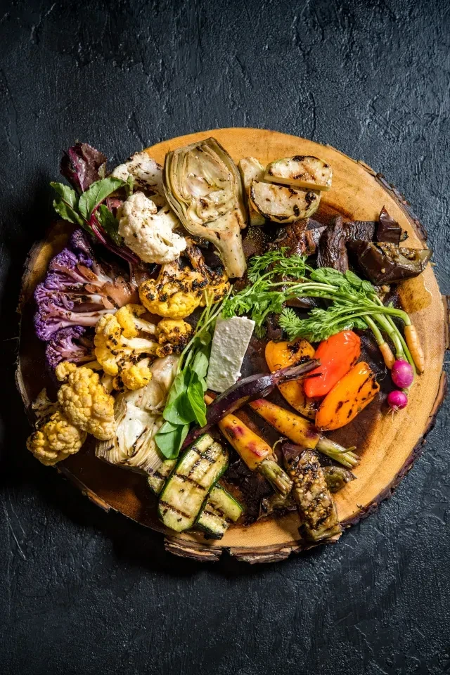 Colorful grilled vegetables, herbs, and white cheese on a rustic board.