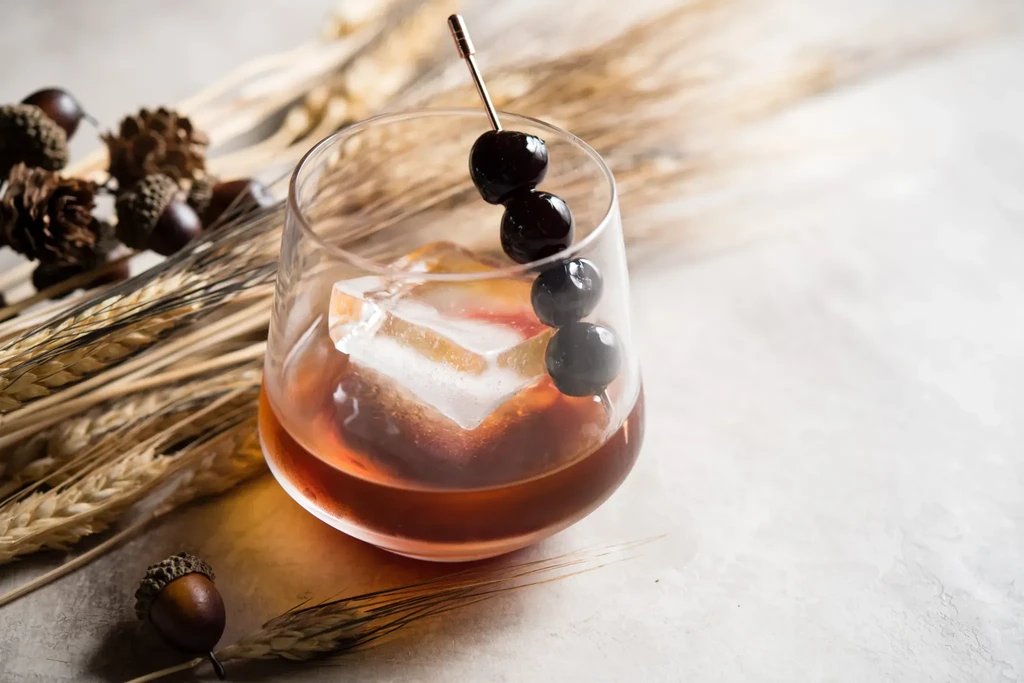 Amber cocktail in stemmed glass with ice, cherries, and autumn decor.