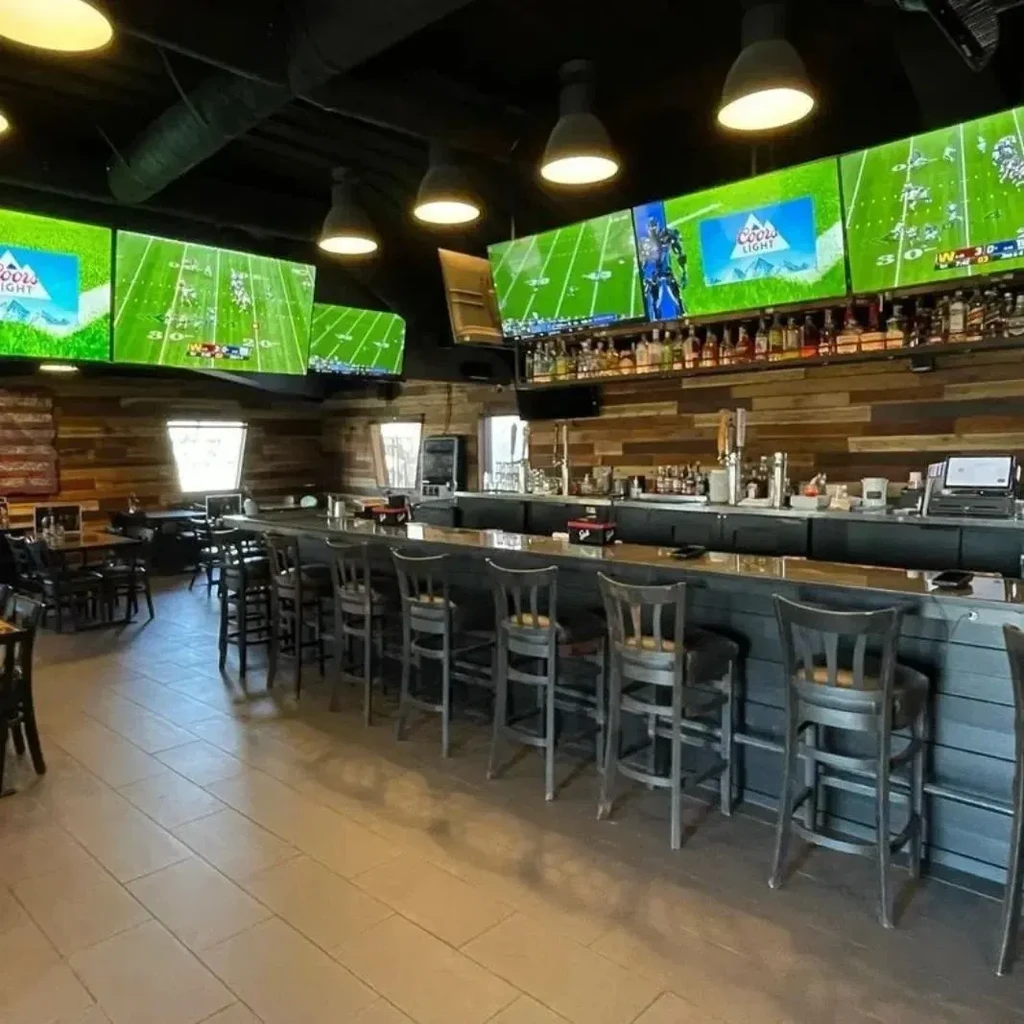 Empty sports bar with a long bar, multiple TVs, and liquor bottles.