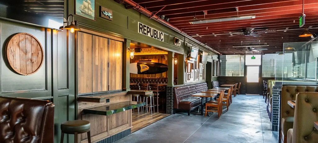 Empty rustic industrial bar and restaurant with booths and exposed ceiling.