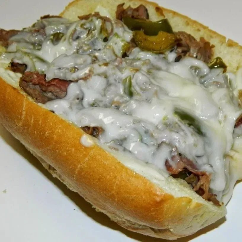 Close-up cheesesteak with melted cheese and green peppers.