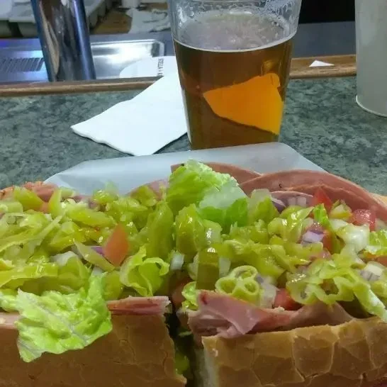 Generously filled deli sub sandwich with vegetables and beer on a counter.