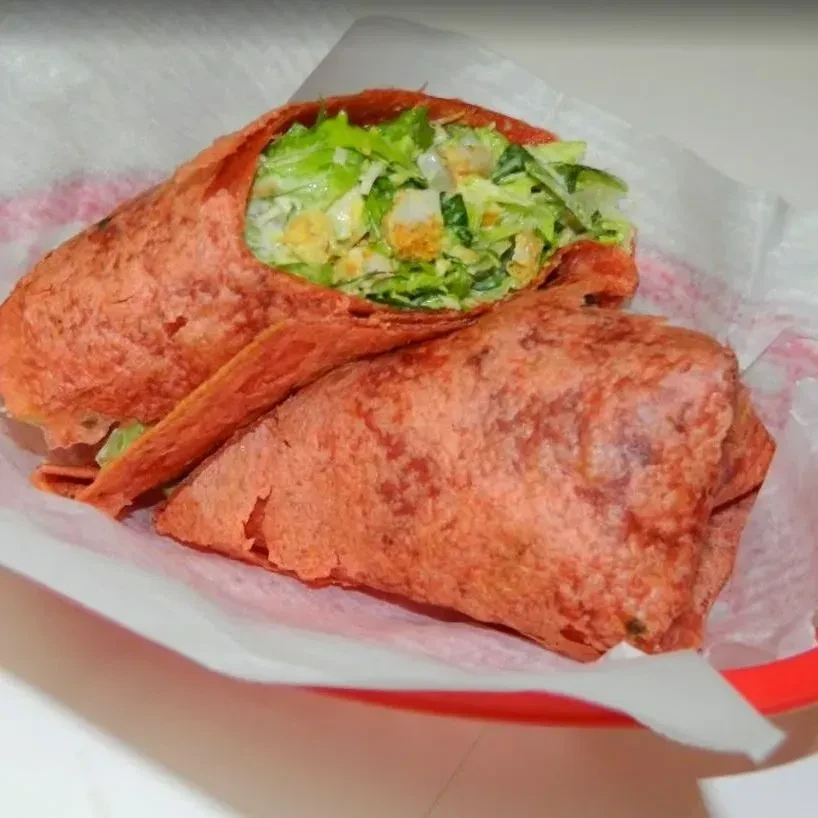 Reddish-orange Caesar salad wrap, cut in half, in a red basket.