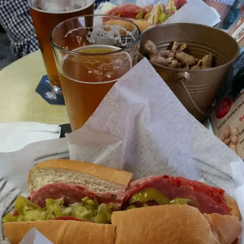 Close-up of a submarine sandwich, two beers, and peanuts.
