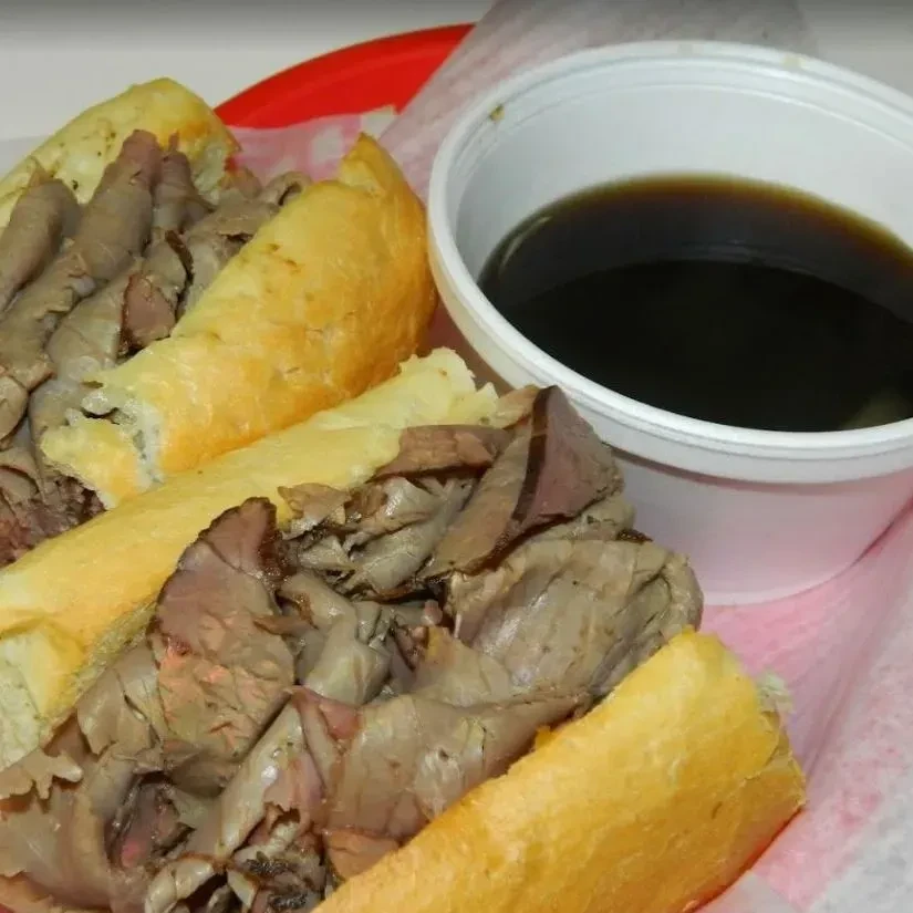Thinly sliced roast beef sandwich in red basket with au jus.