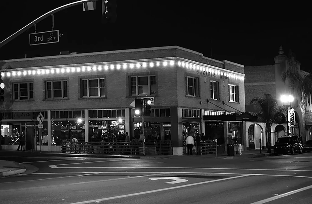 Black and white urban street corner with a busy, lit restaurant.