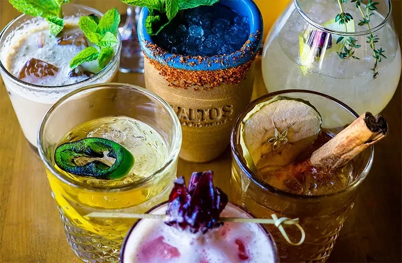 Six distinct cocktails with varied garnishes on a rustic wooden table.