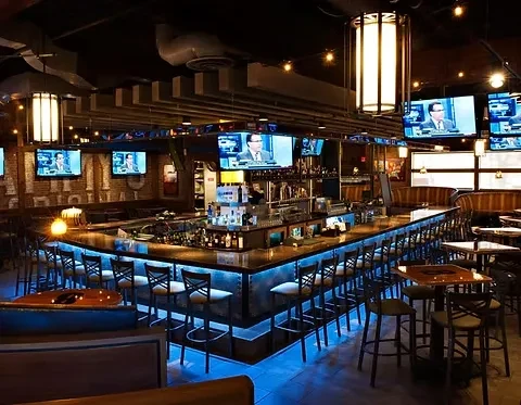 Empty modern bar with U-shaped LED-lit bar and multiple TV screens.