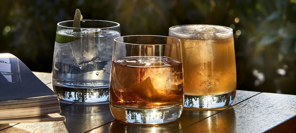 Three iced drinks on a wooden table with blurred green foliage.