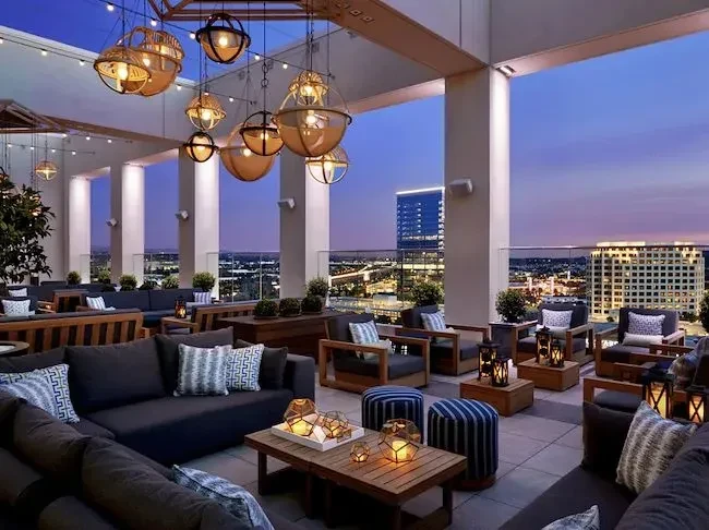 Empty rooftop lounge at twilight, warm lighting, comfortable seating, city view.