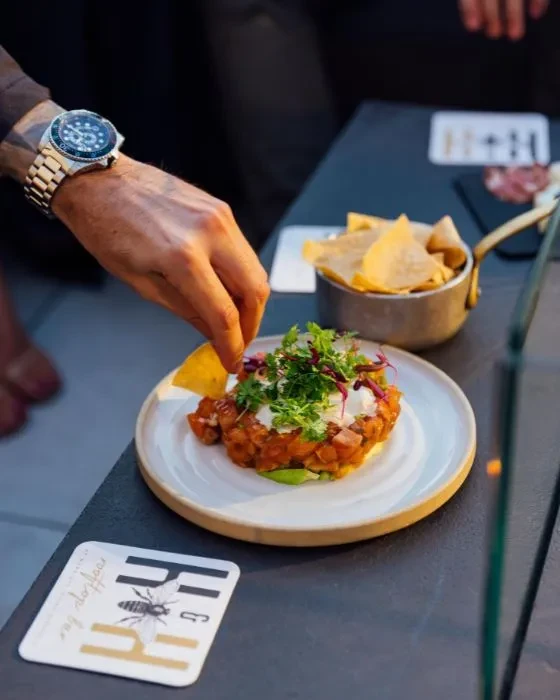 Hand reaching for tortilla chip from ceviche dish at bar.