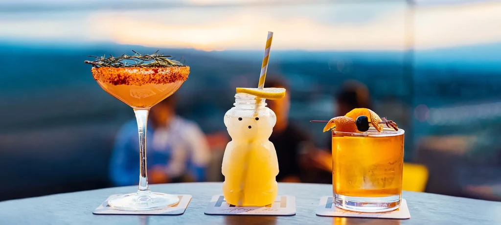 Three distinct garnished cocktails on a dark table at sunset rooftop.