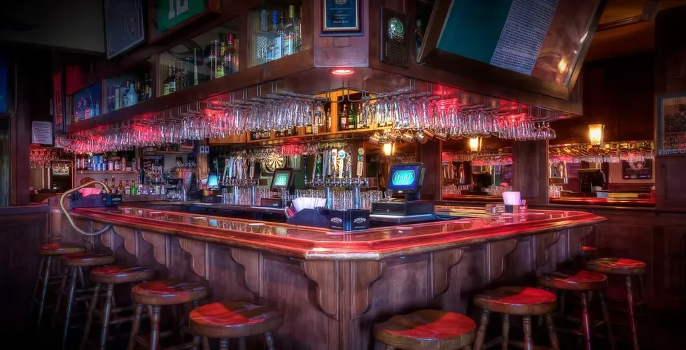 Warm, empty wooden pub bar with bottles, glasses, and decor.