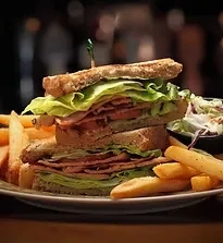 Close-up of a stacked club sandwich, fries, and coleslaw on a plate.