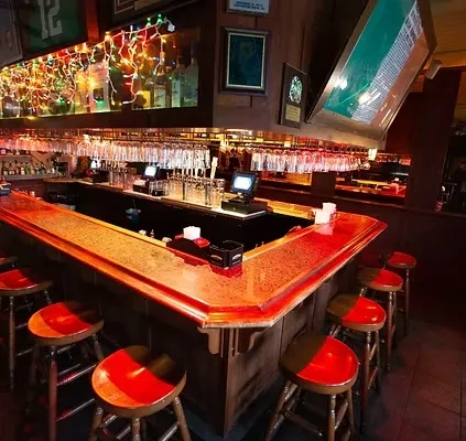 L-shaped wooden bar, red stools, brightly lit liquor display.