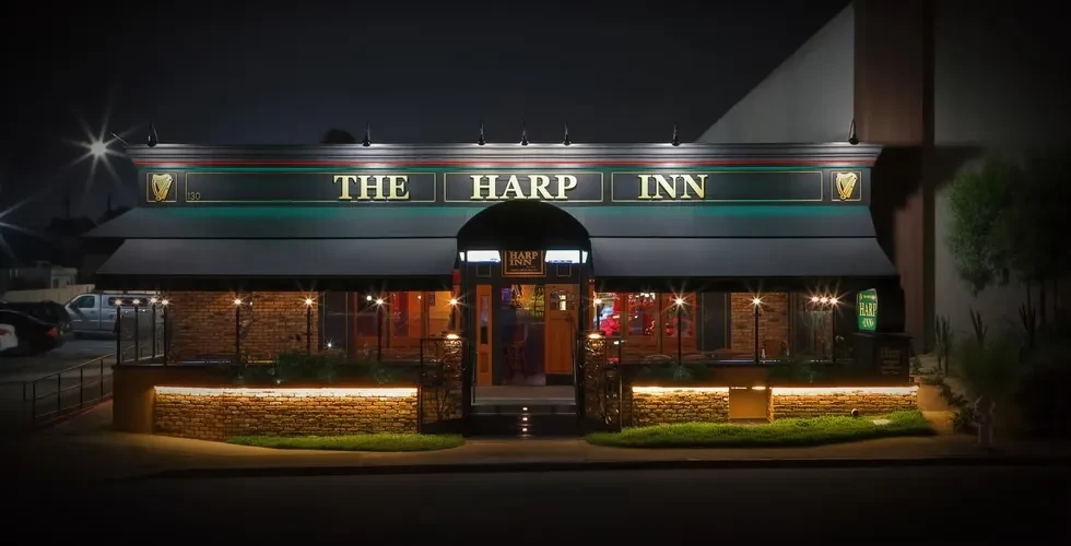 The Harp Inn's well-lit brick exterior and signs at night.