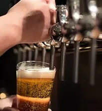 Close-up of hand pouring frothy dark beer from a tap.