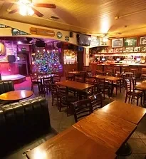 Warmly lit pub with wooden tables, a bar, and a stage.