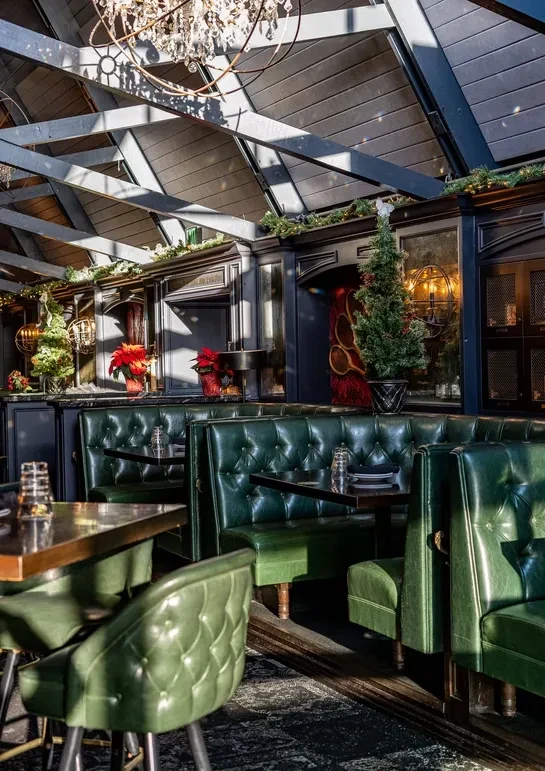 Tufted green booths and a chandelier decorate a festive restaurant interior.