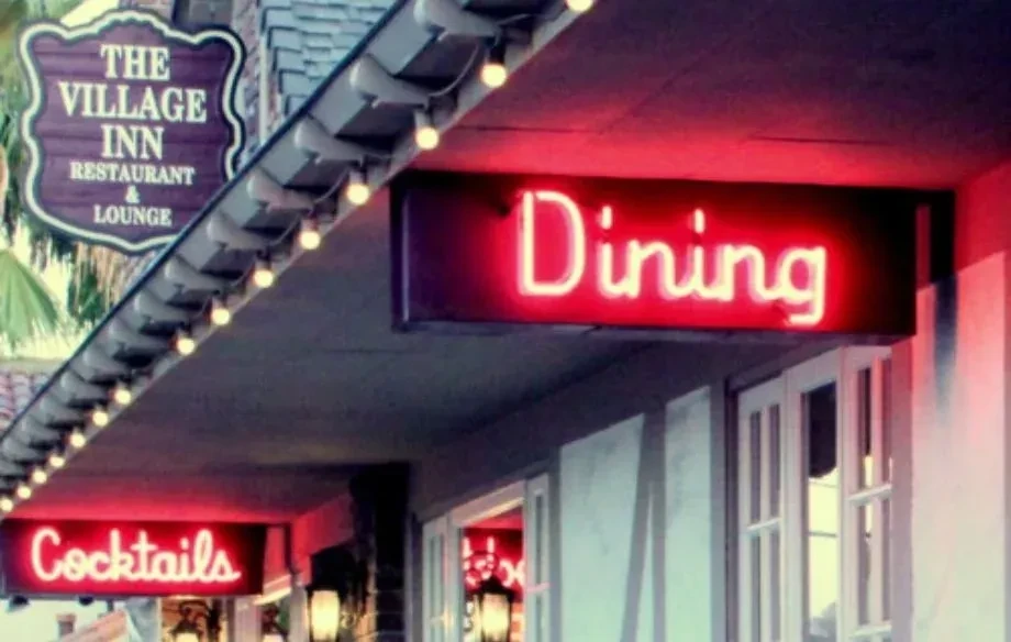 Village Inn restaurant facade with 'Dining' and 'Cocktails' neon signs.