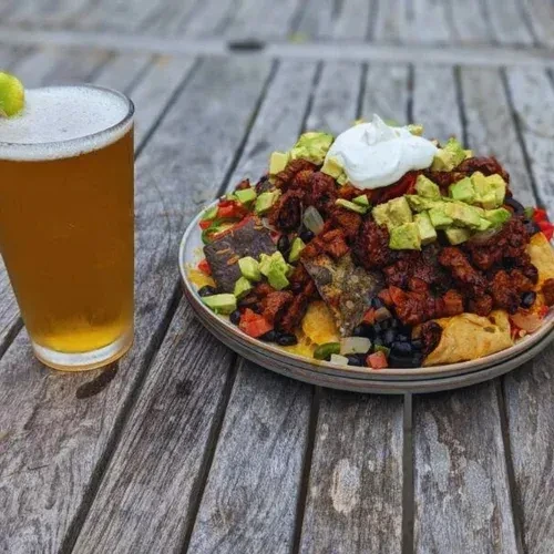 Generous nachos with meat and avocado, alongside a beer with lime.