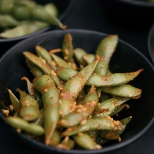 Bright green seasoned edamame pods in a black bowl.