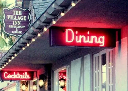 Exterior of The Village Inn Restaurant and Lounge with glowing neon signs.