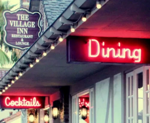 Exterior of The Village Inn Restaurant & Lounge with neon signs.