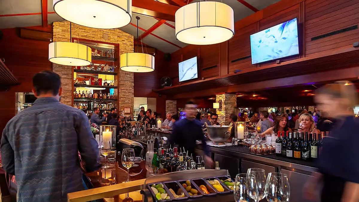 Busy interior bar with drum pendant lights and stocked liquor shelves
