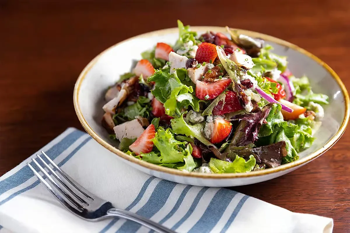 Green salad with strawberries, chicken and blue cheese in white bowl