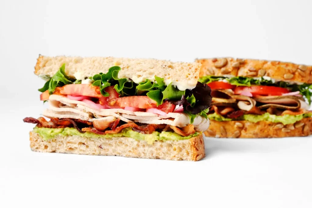 Robust seeded sandwich with avocado, bacon, deli meat, tomato, greens.
