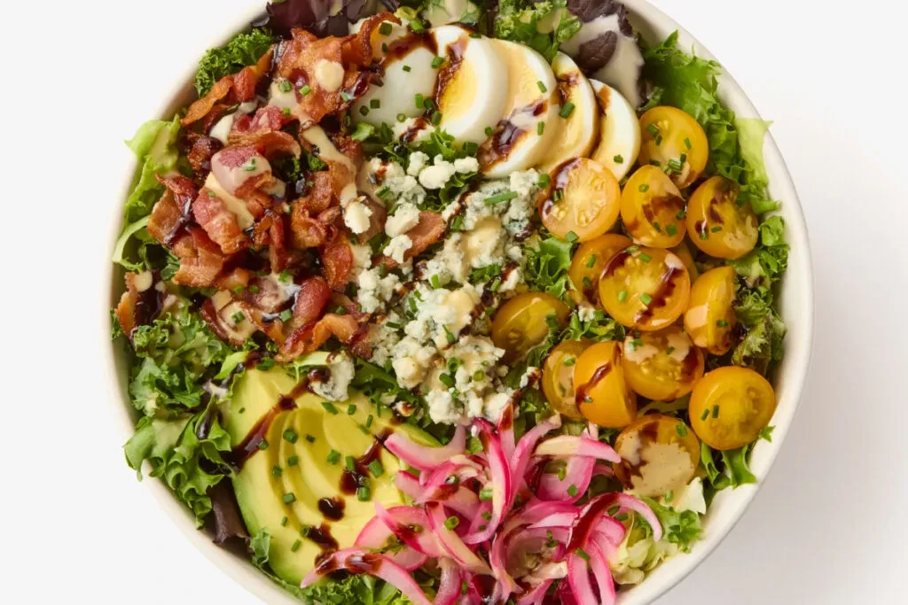 Overhead view: colorful salad with bacon, egg, avocado, and blue cheese.