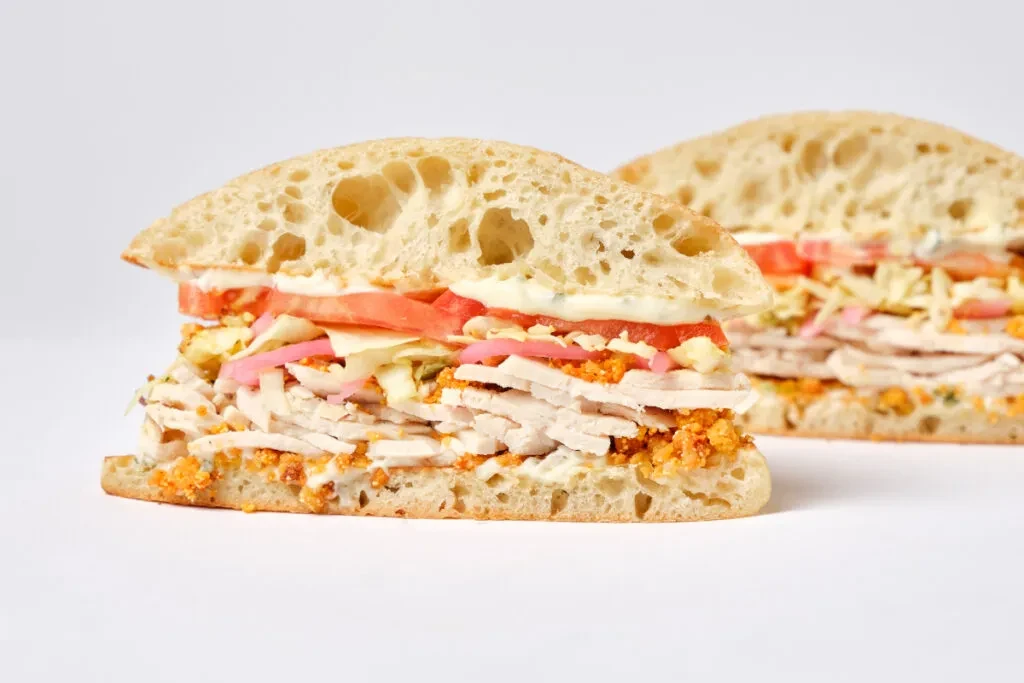 Diagonally cut ciabatta sandwich with turkey, pink onions, lettuce, and tomato.