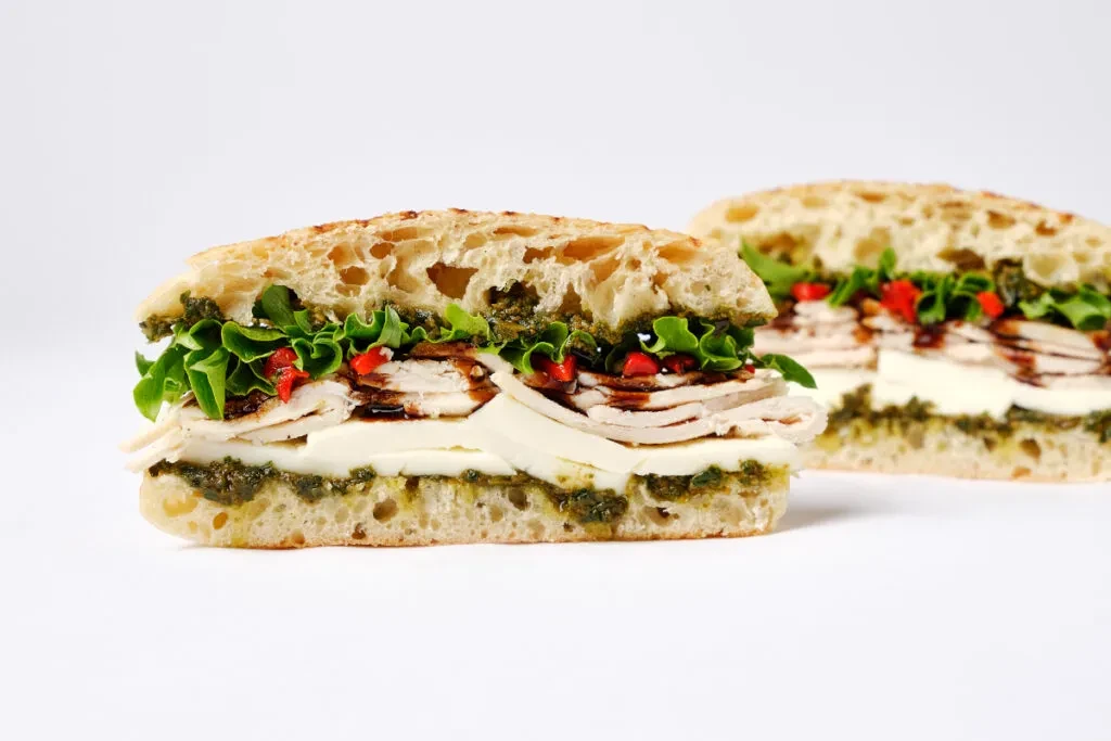 Sliced ciabatta sandwich with pesto, mozzarella, turkey, lettuce, balsamic drizzle.